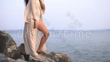 女孩模特穿着一件长裙子站在靠海的石头上。 慢动作。 高清高清